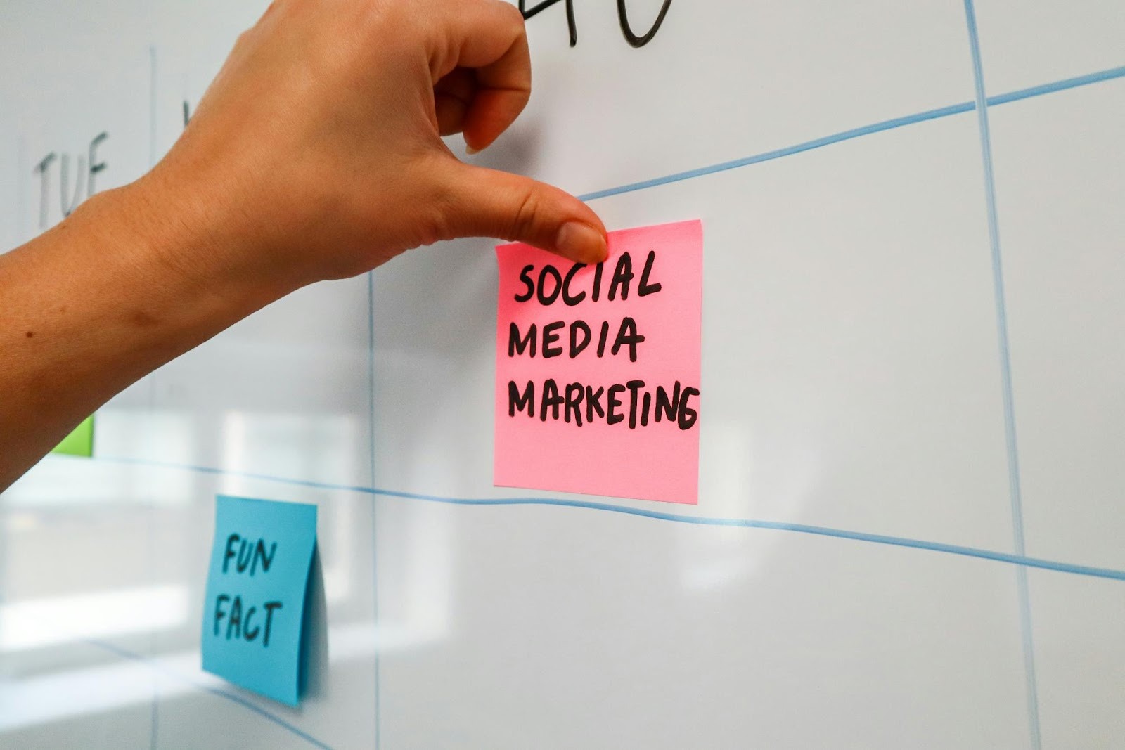 Hand placing a "Social Media Marketing" sticky note on a planning board, representing content calendar management and strategic organization.