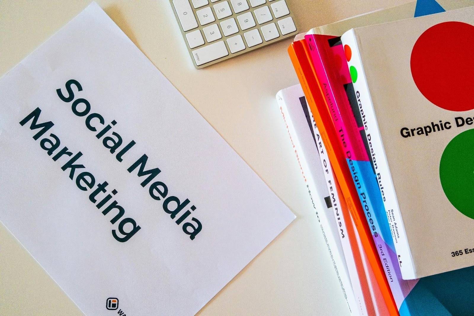 Stack of graphic design books next to a "Social Media Marketing" printout, highlighting the need for visual creativity in marketing strategy.