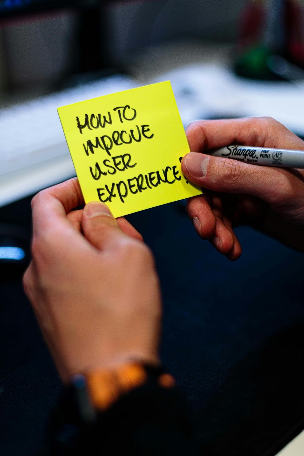 Hands holding a sticky note asking "How to improve user experience," a critical factor for SEO and website conversion rates.